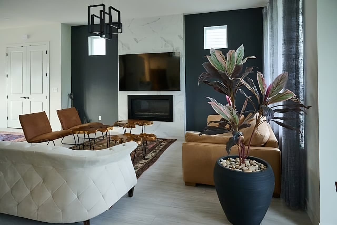 Modern Montreal living room with dark accent walls, mid-century leather chairs, tufted cream sofa, and a contemporary fireplace with mounted TV.